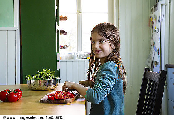 Smiling girl cutting tomatoes on chopping board in kitchen