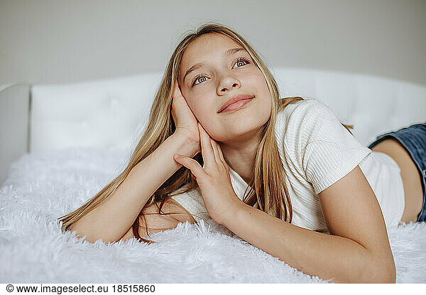 Smiling girl day dreaming lying on bed at home