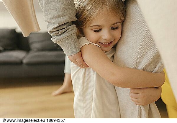 Smiling girl embracing grandmother's leg at home