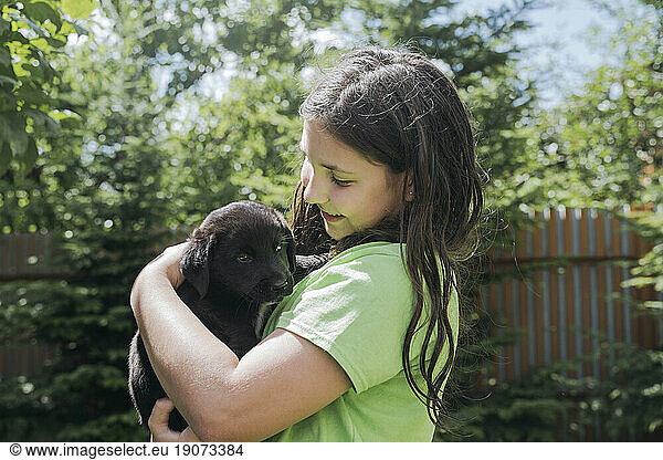 Smiling girl embracing puppy in back yard
