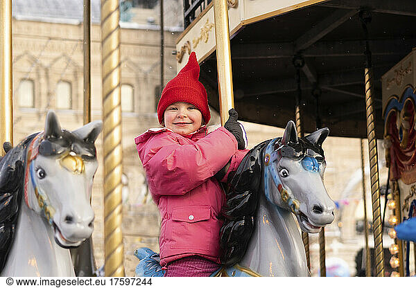 Smiling girl enjoying carousel horse ride at Christmas market