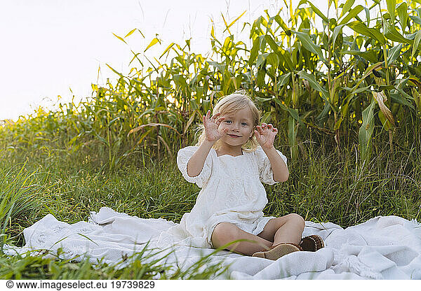 Smiling girl gesturing and sitting on blanket in front of plants