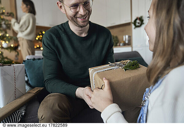 Smiling girl giving Christmas gift to father at home