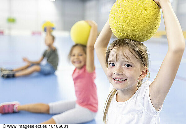 Smiling girl holding ball on head at school sports court