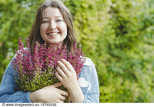 Smiling girl holding heather flowers in front of plants