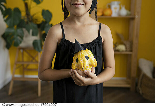 Smiling girl holding painted pumpkin at home