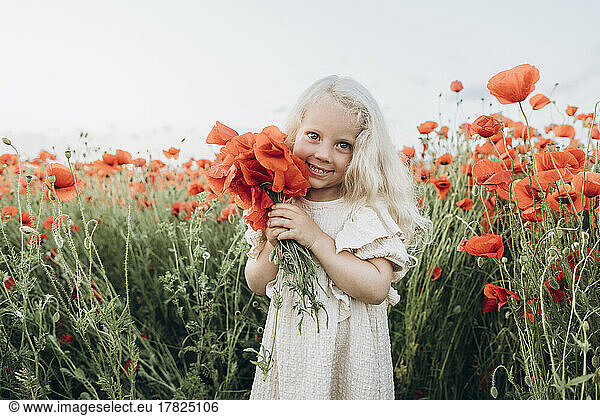 Smiling girl holding red flower in poppy field