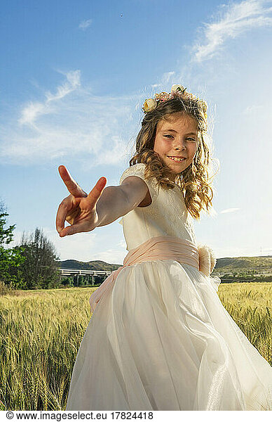 Smiling girl in communion dress gesturing peace sign on field