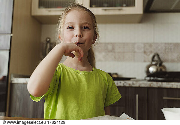 Smiling girl licking finger in kitchen at home