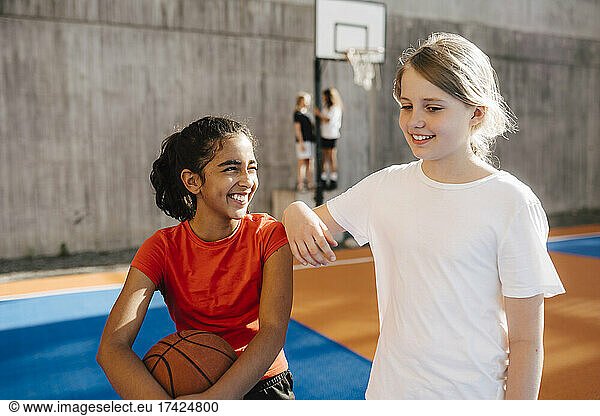 Smiling girl looking at female friend in sports court