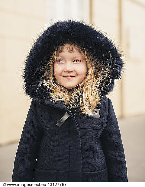 Smiling girl looking away while wearing fur coat outdoors