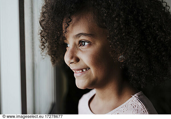 Smiling girl looking through window at home