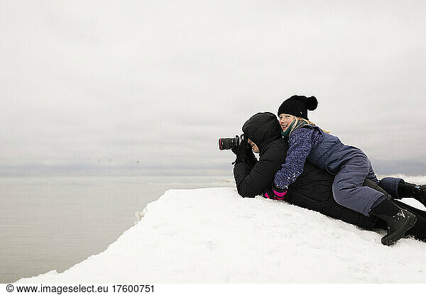 Smiling girl lying on mother photographing through camera in winter