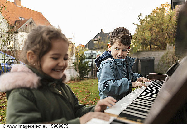 Smiling girl playing piano with brother in backyard