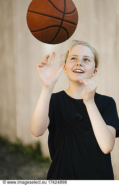 Smiling girl playing with ball at basketball court