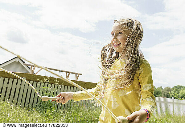 Smiling girl playing with jump rope at backyard on sunny day