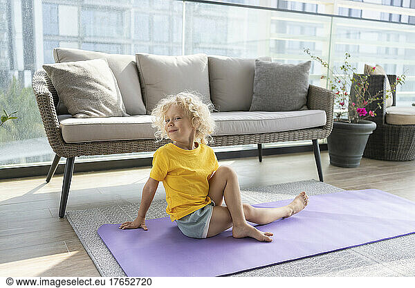 Smiling girl practicing seated twist in front of sofa at home