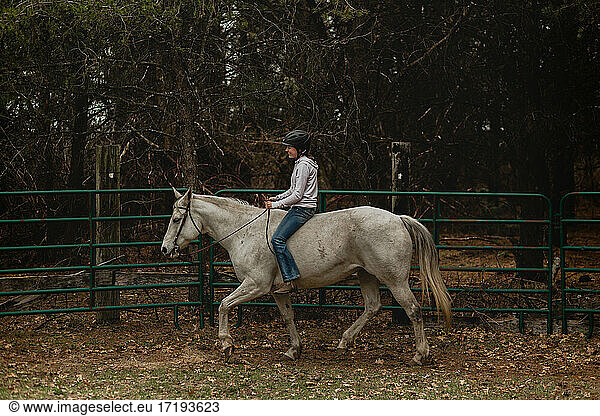 Smiling girl riding grey mare bareback in round pen with head stall