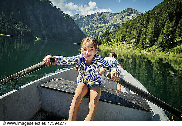 Smiling girl rowing rowboat with brother in background