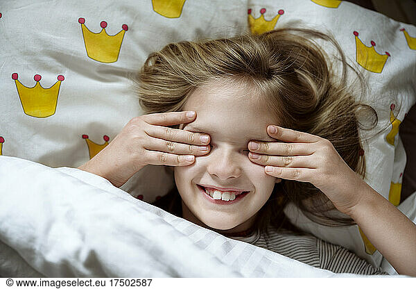 Smiling girl rubbing eyes on bed at home