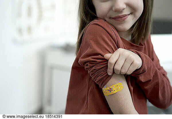 Smiling girl showing adhesive bandage after vaccination in clinic