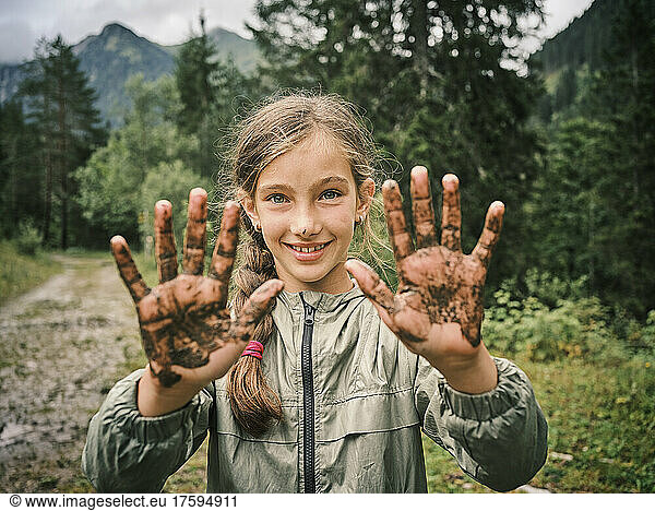 Smiling girl showing muddy hands in forest