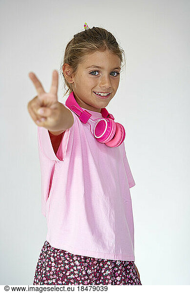 Smiling girl showing peace sign against white background