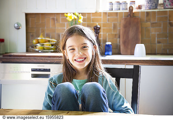 Smiling girl sitting at kitchen table and looking at camera