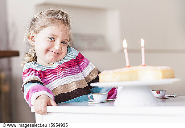 Smiling girl sitting at table with birthday cake