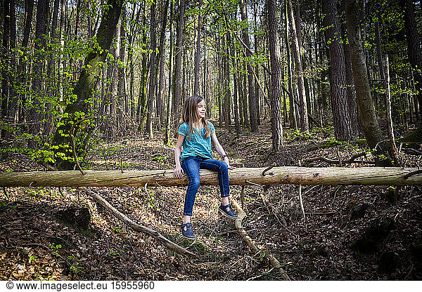 Smiling girl sitting on deadwood in forest