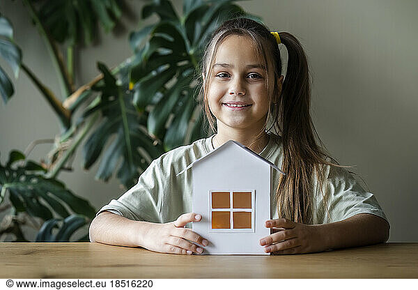 Smiling girl sitting with green home model at table