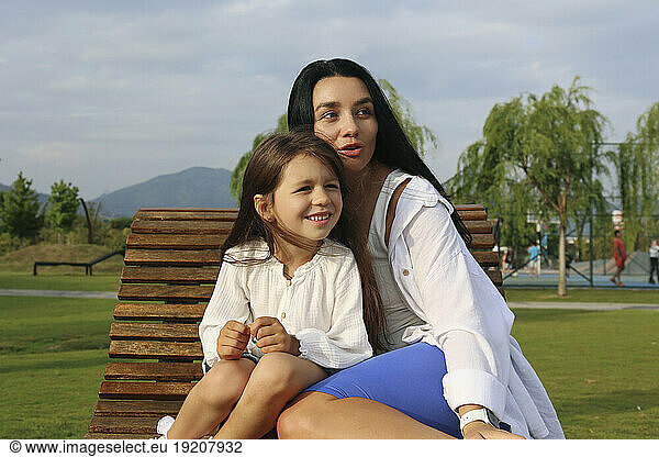 Smiling girl sitting with mother on lounge chair in park