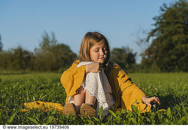Smiling girl smelling flower and sitting on grass