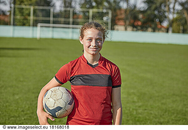Smiling girl standing with soccer ball on sunny day