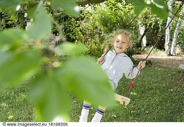 Smiling girl swinging on swing in garden