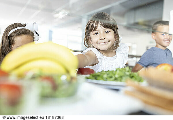 Smiling girl taking banana at lunch break in school cafeteria