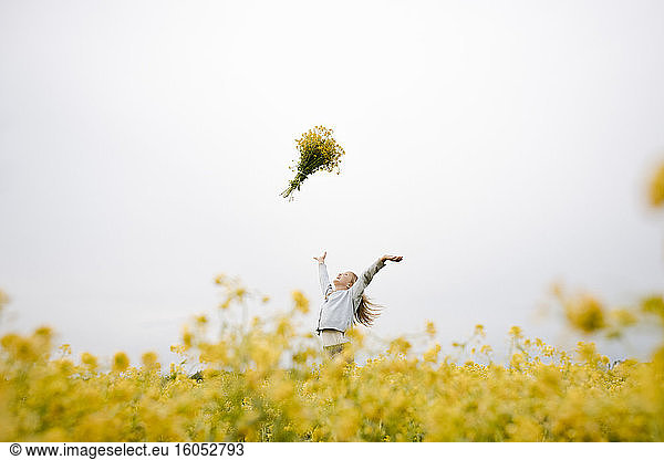 Smiling girl throwing bouquet of rape flowers up