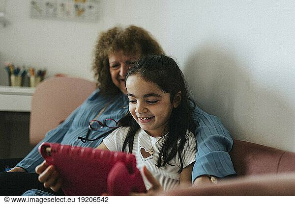 Smiling girl using digital tablet with grandmother at home