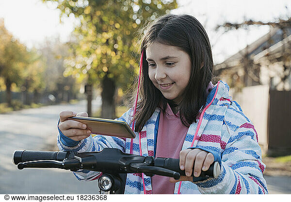 Smiling girl using smart phone to rent electric scooter