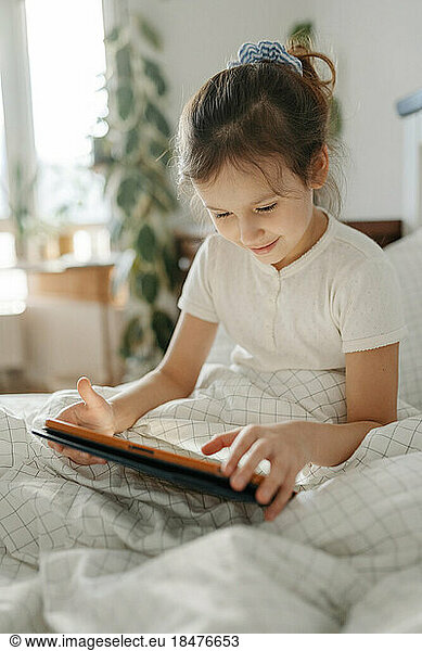 Smiling girl using tablet computer in bedroom at home