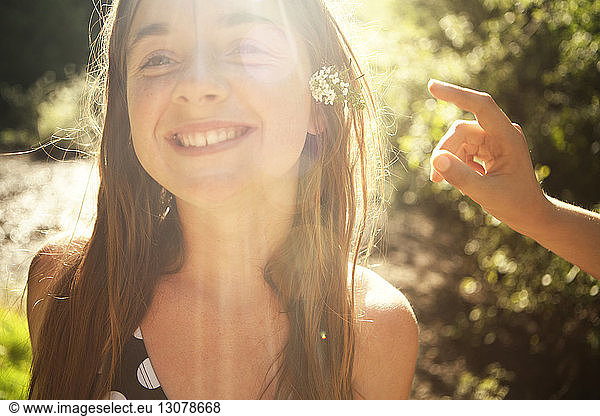 Smiling girl wearing flowers in forest on sunny day