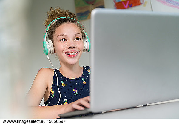Smiling girl wearing headphones using laptop