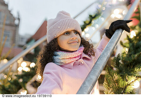 Smiling girl wearing pink knit hat standing near railing