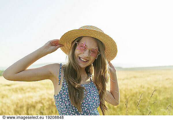 Smiling girl wearing star shaped sunglasses and hat at field
