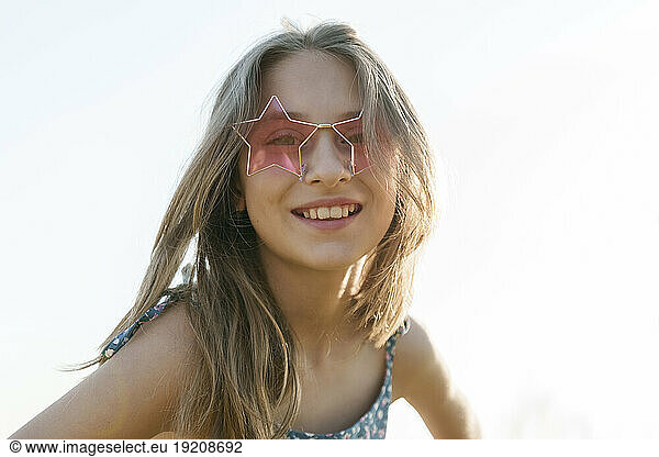 Smiling girl wearing star shaped sunglasses in front of sky
