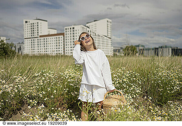 Smiling girl wearing sunglasses holding wicker basket in meadow