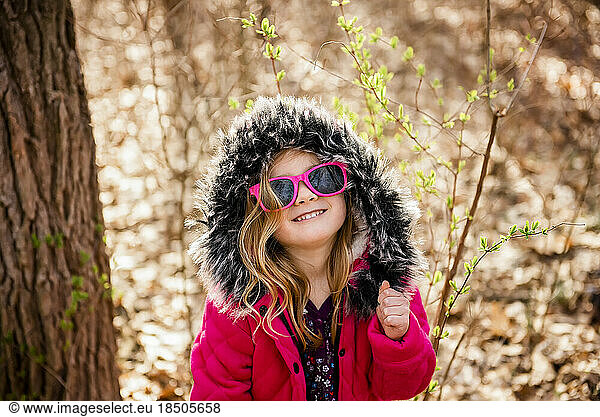 Smiling girl wears sunglasses dancing in woods during Fall
