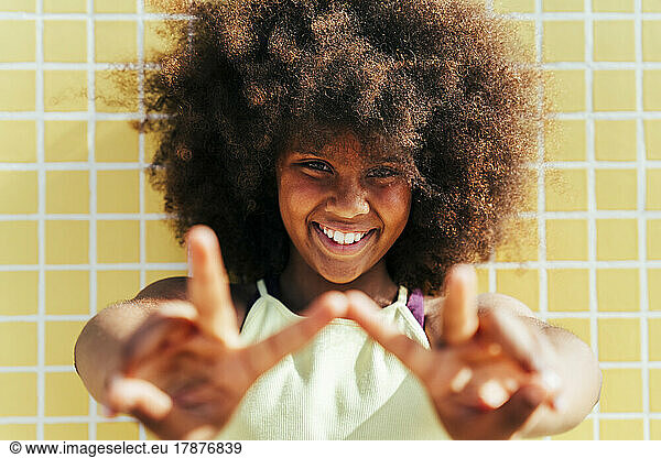 Smiling girl with Afro hairstyle gesturing peace sign