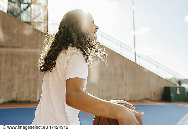 Smiling girl with ball at basketball court on sunny day