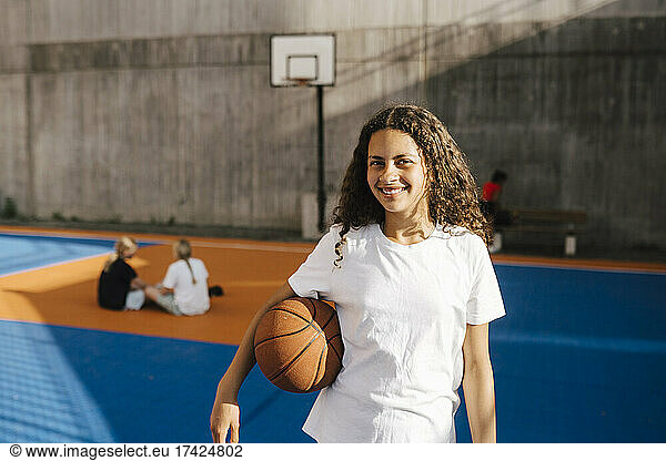 Smiling girl with basketball at basketball court
